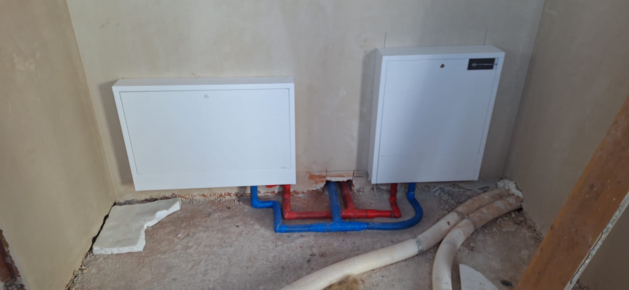 Rozdzielacze ogrzewania podłogowego z rurami w kolorze niebieskim i czerwonym, zamontowane na ścianie w Częstochowie. Widoczne elementy instalacji przed zalaniem posadzki.