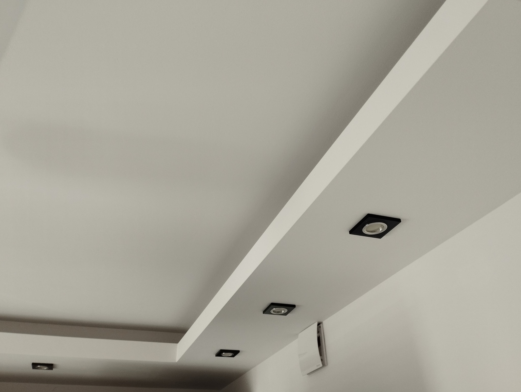 Biały sufit z wbudowanymi, kwadratowymi lampami w czarnych oprawach, widoczne elementy wentylacji.