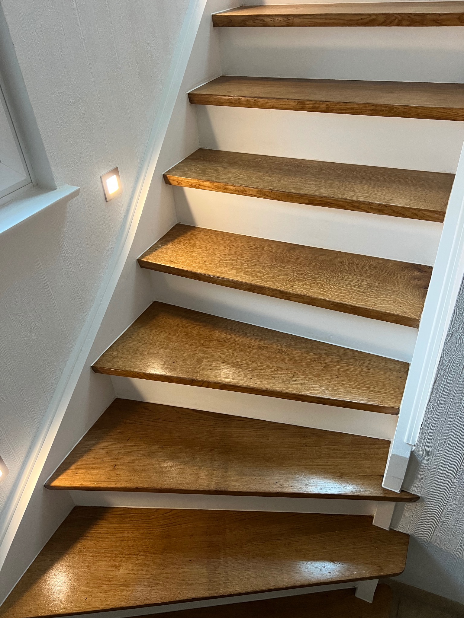 Drewniane schody w Słupsku z podświetleniem LED w ścianie, białe boki. Widok z dołu, ukazujący detale wykończenia i naturalny odcień drewna.