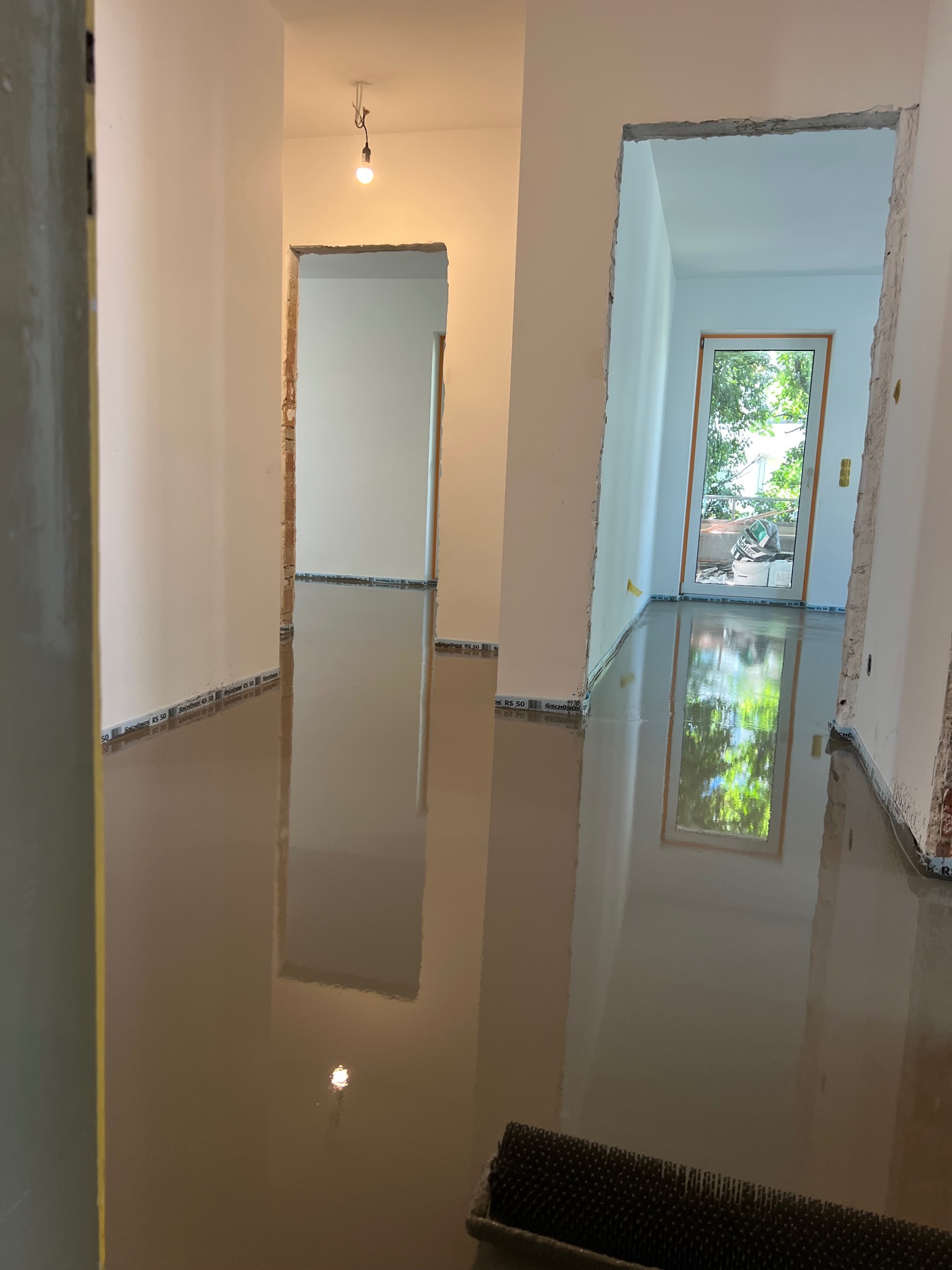 Wnętrze w trakcie wylewania samopoziomującej wylewki. Widoczne przygotowane ściany z widocznymi śladami po poprzednich pracach i narzędzie do rozprowadzania wylewki.