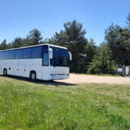 Biały autokar turystyczny zaparkowany na trawiastym terenie w pobliżu lasu, widoczny znak firmowy 'Ruban Bleu' na boku pojazdu.