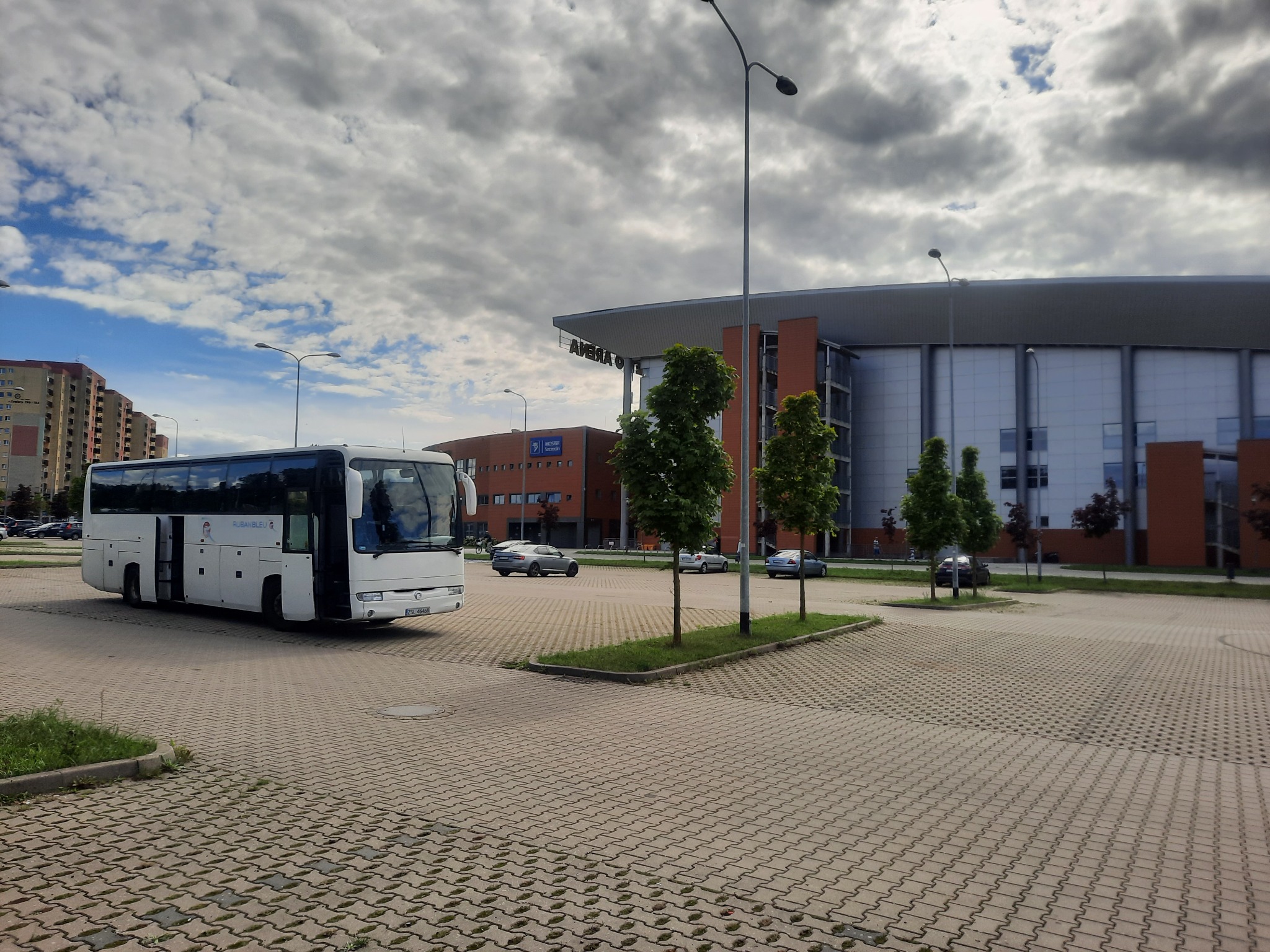 Biały autokar turystyczny z otwartymi drzwiami na parkingu przed Areną, pochmurne niebo