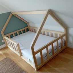 Drewniane ł&oacute;żko dziecięce w kształcie domku z białym materacem na drewnianej podłodze w pokoju z zieloną ścianą.