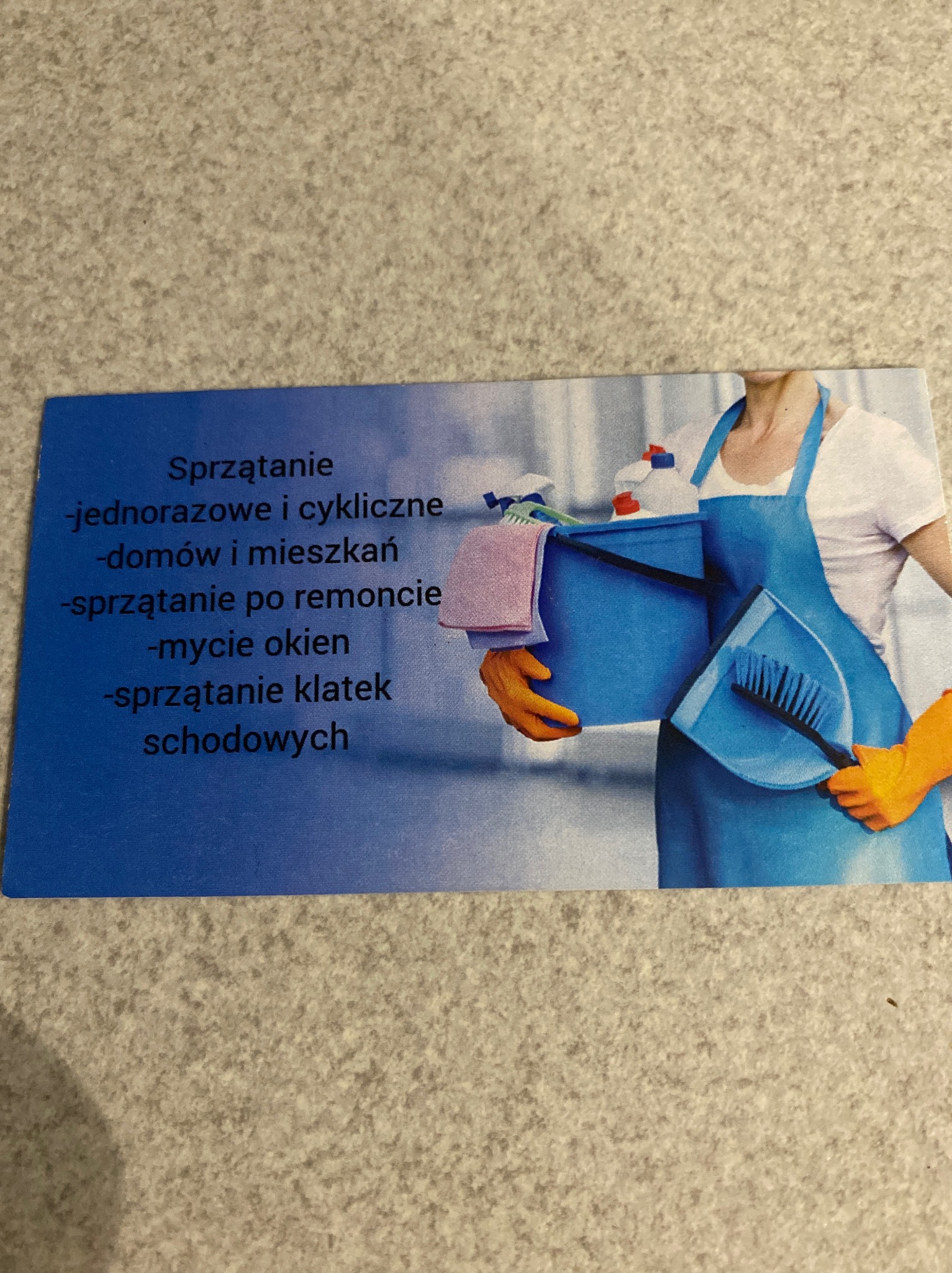 Zdjęcie wizytówki firmy oferującej usługi porządkowe: kobieta w niebieskim fartuchu trzymająca niebieskie wiadro ze środkami czystości i szczotką.