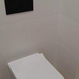 Alfa Goshkar Ahmadov - Nowoczesna, podwieszana toaleta z czarnym panelem spłukującym na białych, poziomych płytkach i drewnopodobną podłogą.