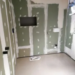 Wnętrze łazienki w trakcie szpachlowania: ściany z płyt gipsowo-kartonowych z widocznymi łączeniami i wnęką, wylewka samopoziomująca na podłodze, widoczne elementy instalacji hydraulicznej.