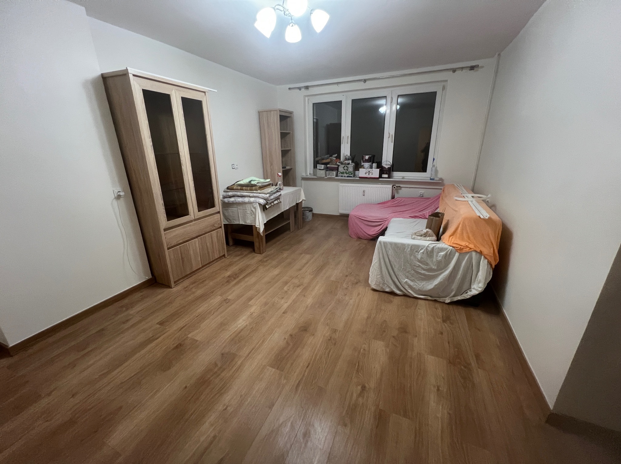 Wykończone panele podłogowe w pokoju w Szczecinie, widok na drewnianą podłogę, meble i zakryte meble. Jasne wnętrze, ciepłe oświetlenie.