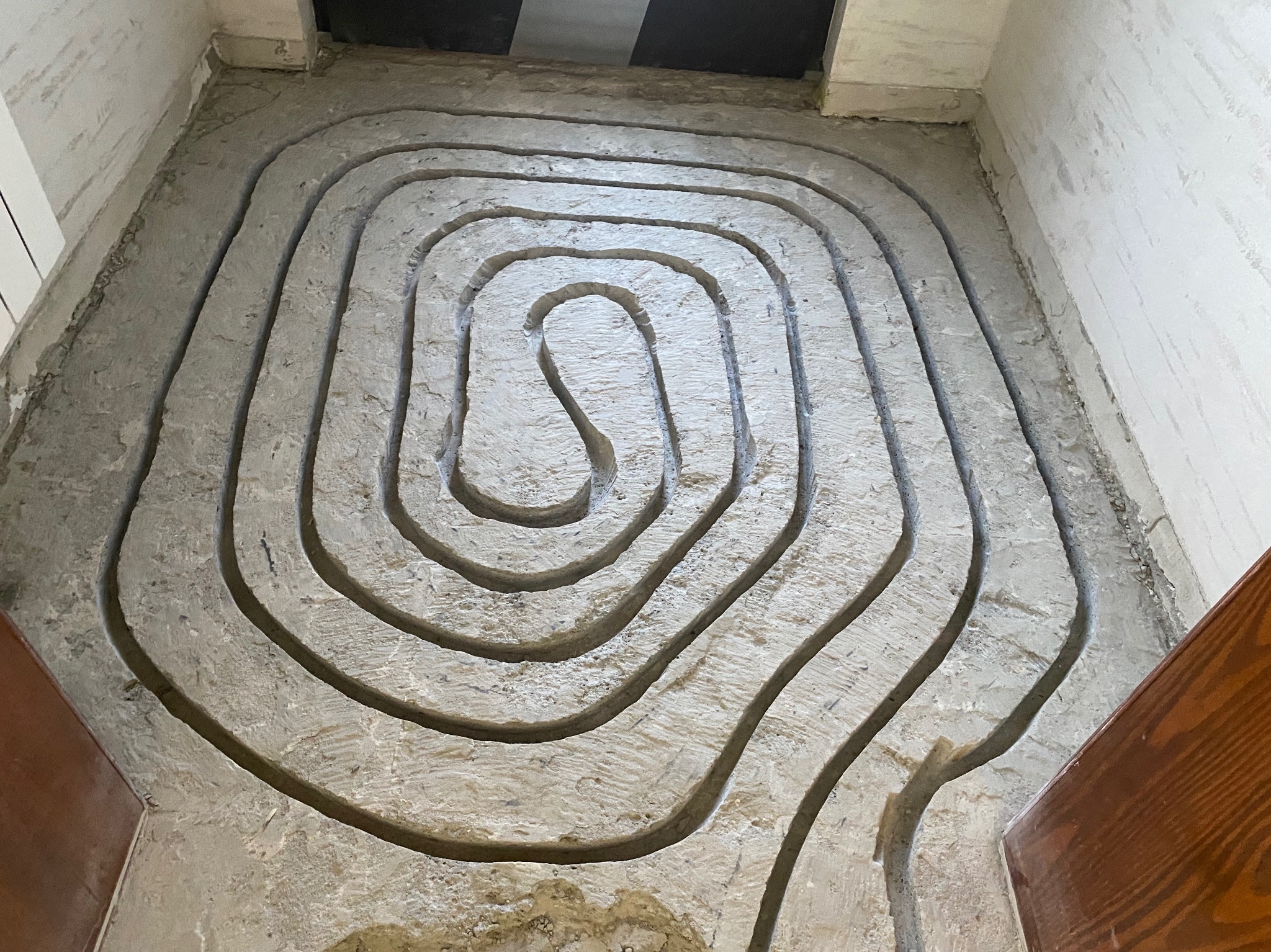 Wyfrezowane kanały w podkładzie podłogowym, przygotowane pod montaż instalacji ogrzewania podłogowego. Widok z góry, surowy beton, przygotowanie do dalszych prac.