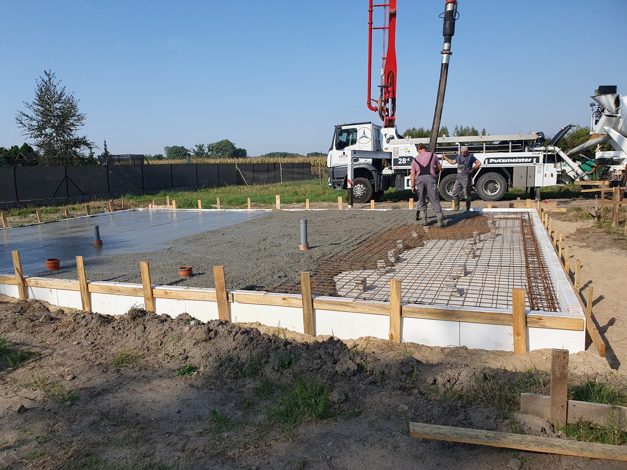 Wylewanie fundamentów pod dom jednorodzinny z użyciem pompy do betonu Putzmeister, widoczne zbrojenie i szalunki.