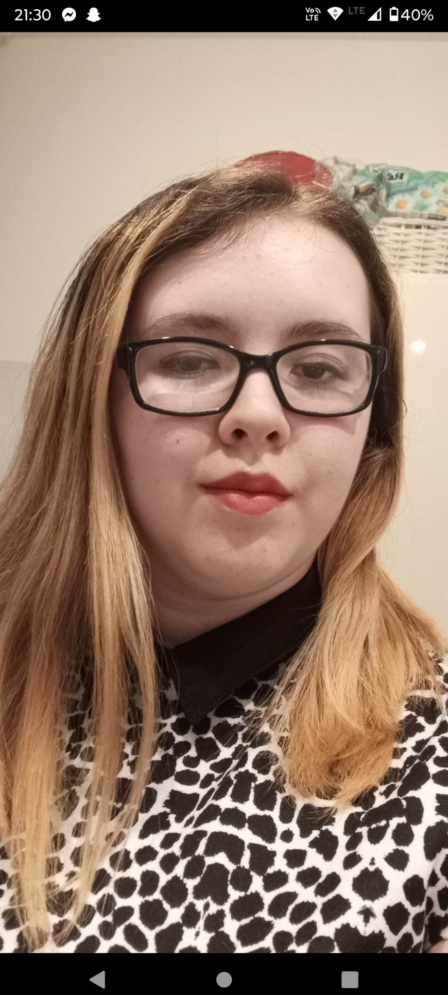 Portret kobiety w okularach, z blond włosami i bluzką w panterkę, z widocznym fragmentem koszyka wiklinowego w tle.