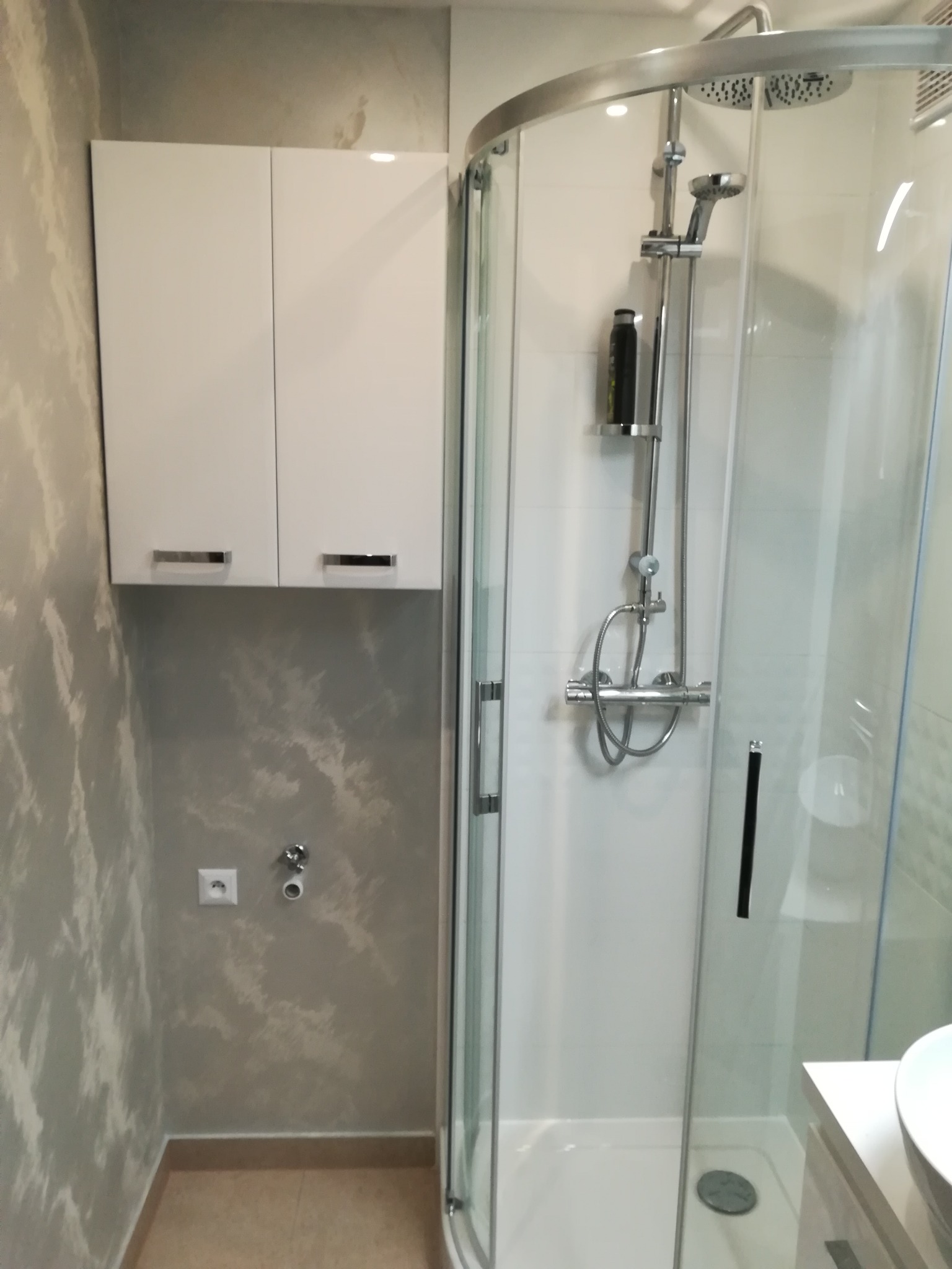 Wykończona łazienka z kabiną prysznicową narożną, szafką wiszącą i dekoracyjną szarą ścianą imitującą chmury.