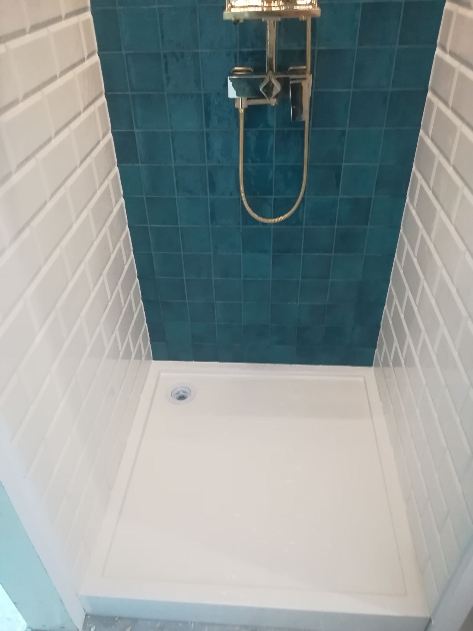 Wykończona kabina prysznicowa w Gdyni z białą brodzikiem, jasnoszarymi płytkami ściennymi ułożonymi w cegiełkę i turkusowymi płytkami na suficie, z zamontowaną złotą armaturą.