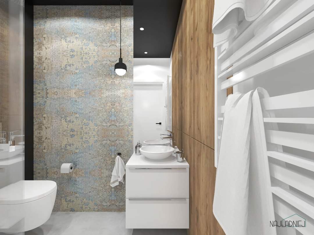 Nowoczesna łazienka z wzorzystą ścianą, wiszącą lampą i drewnianymi panelami, biała umywalka nablatowa na szafce, grzejnik drabinkowy z powieszonym ręcznikiem.