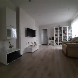 Jasne wnętrze salonu po remoncie: biała cegła na ścianie, podłoga z paneli, białe meble i regał z książkami.