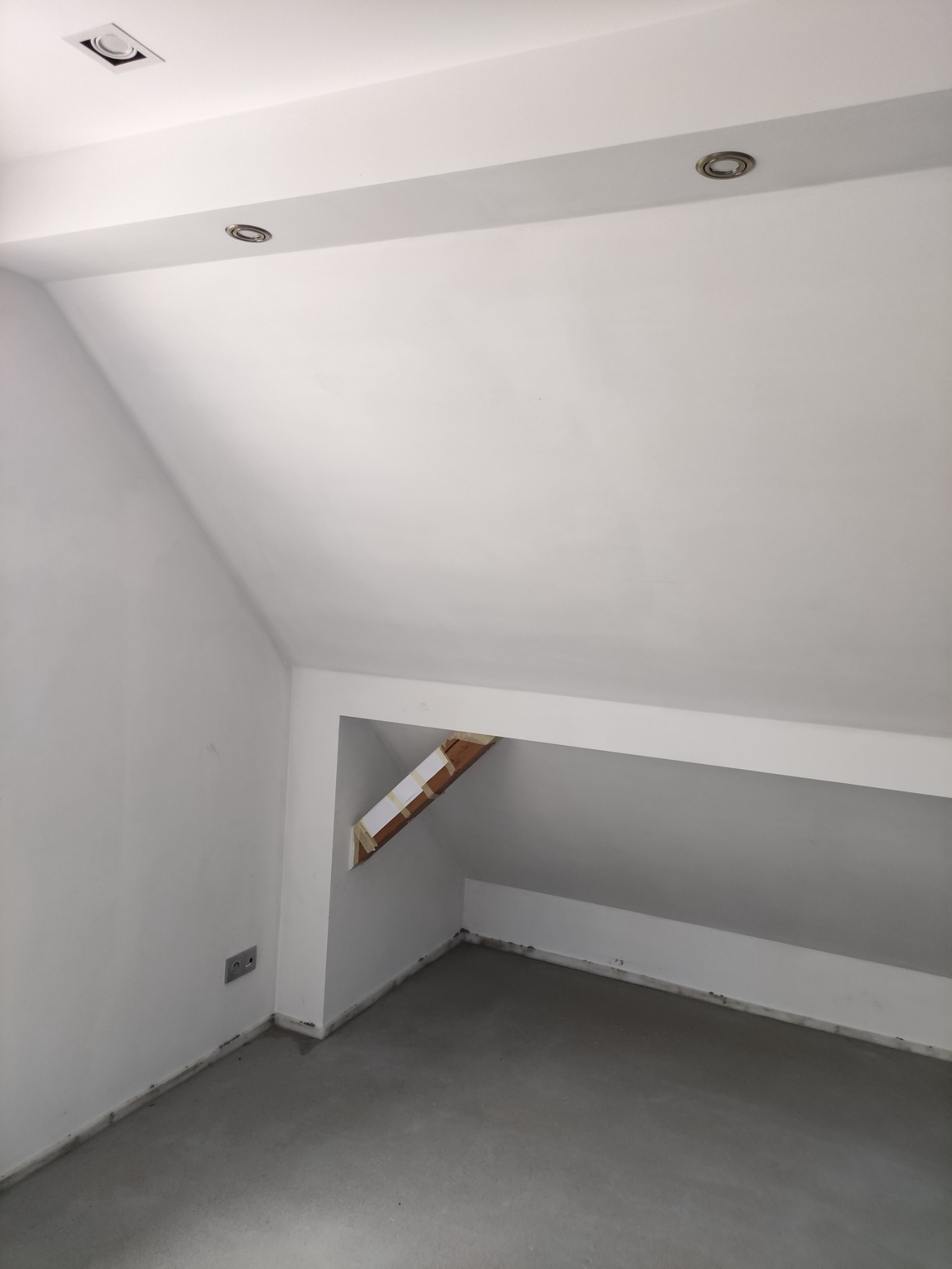 Poddasze po wylewce, ściany pomalowane na biało, widoczne przygotowania do zabudowy wnęki, zabezpieczony element drewniany.
