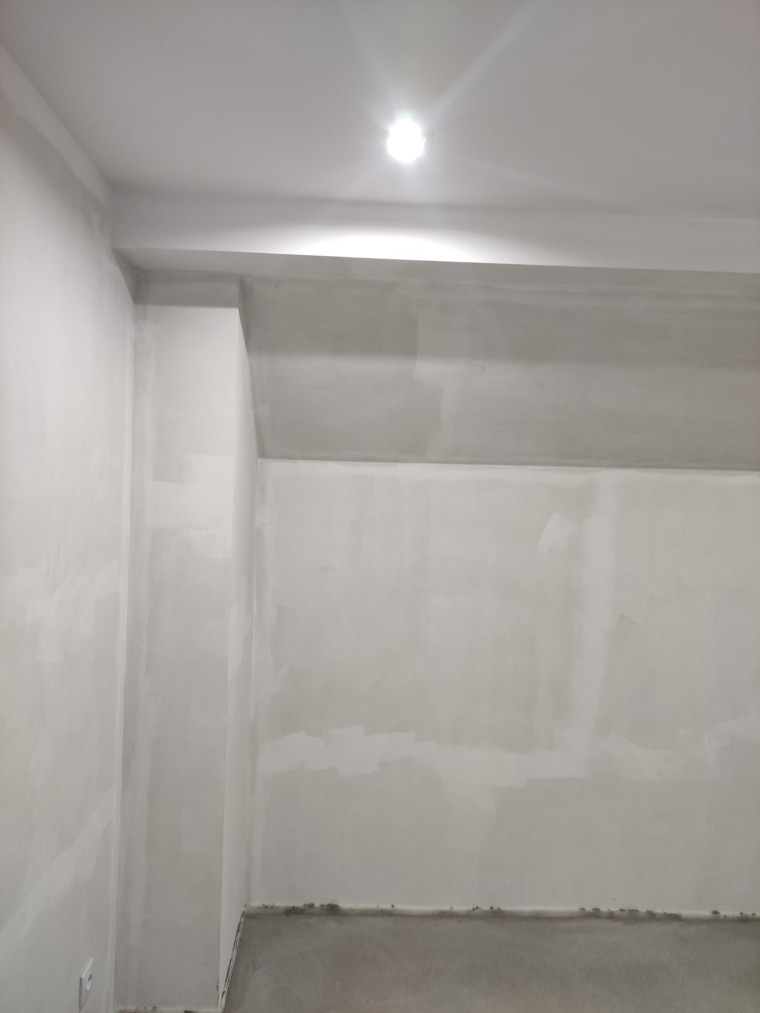 Świeżo wyszpachlowane ściany i sufit w pomieszczeniu z widocznym punktowym oświetleniem sufitowym, przygotowane do dalszych prac wykończeniowych.