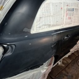 Prywatnie - Przygotowanie samochodu do lakierowania: szpachlowana karoseria kombi oklejona gazetami, widoczne ślady szpachli i niedoskonałości lakieru.