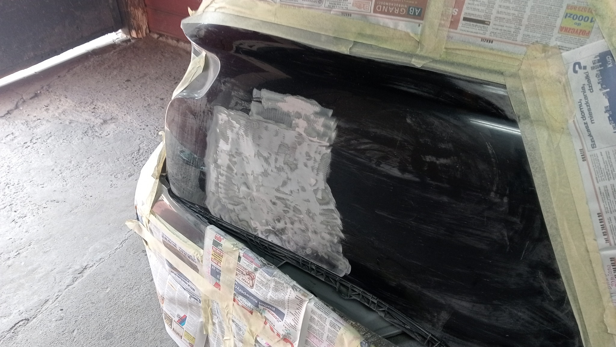 Przygotowanie powierzchni karoserii samochodu do lakierowania: szpachlowanie i maskowanie gazetami z taśmą malarską.