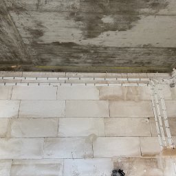 YERIS Instalacje - Białe kable elektryczne ułożone w rzędach na ścianie z białych bloczków, widoczne szare złącza i surowy betonowy sufit. Instalacja w trakcie realizacji.