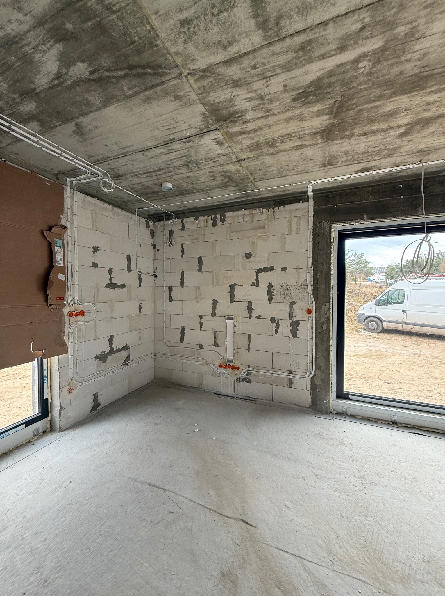 Wnętrze w surowym stanie z rozprowadzoną instalacją elektryczną po ścianach z betonu komórkowego i pod sufitem. Widoczne puszki elektryczne i przewody.