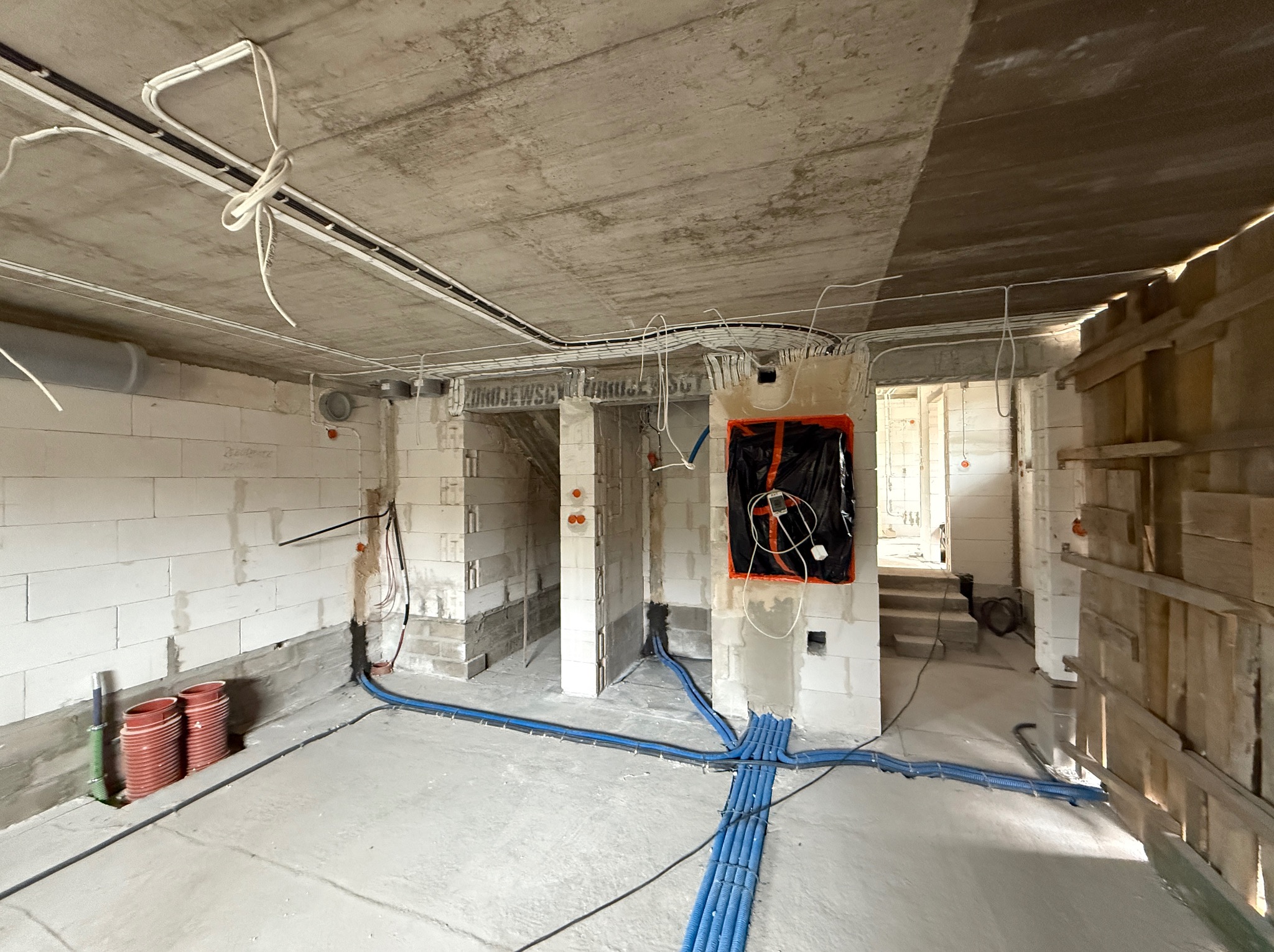 Surowy stan budynku w trakcie prac instalacyjnych: widoczne kable elektryczne, rury hydrauliczne, ściany z betonu komórkowego i surowy betonowy strop.