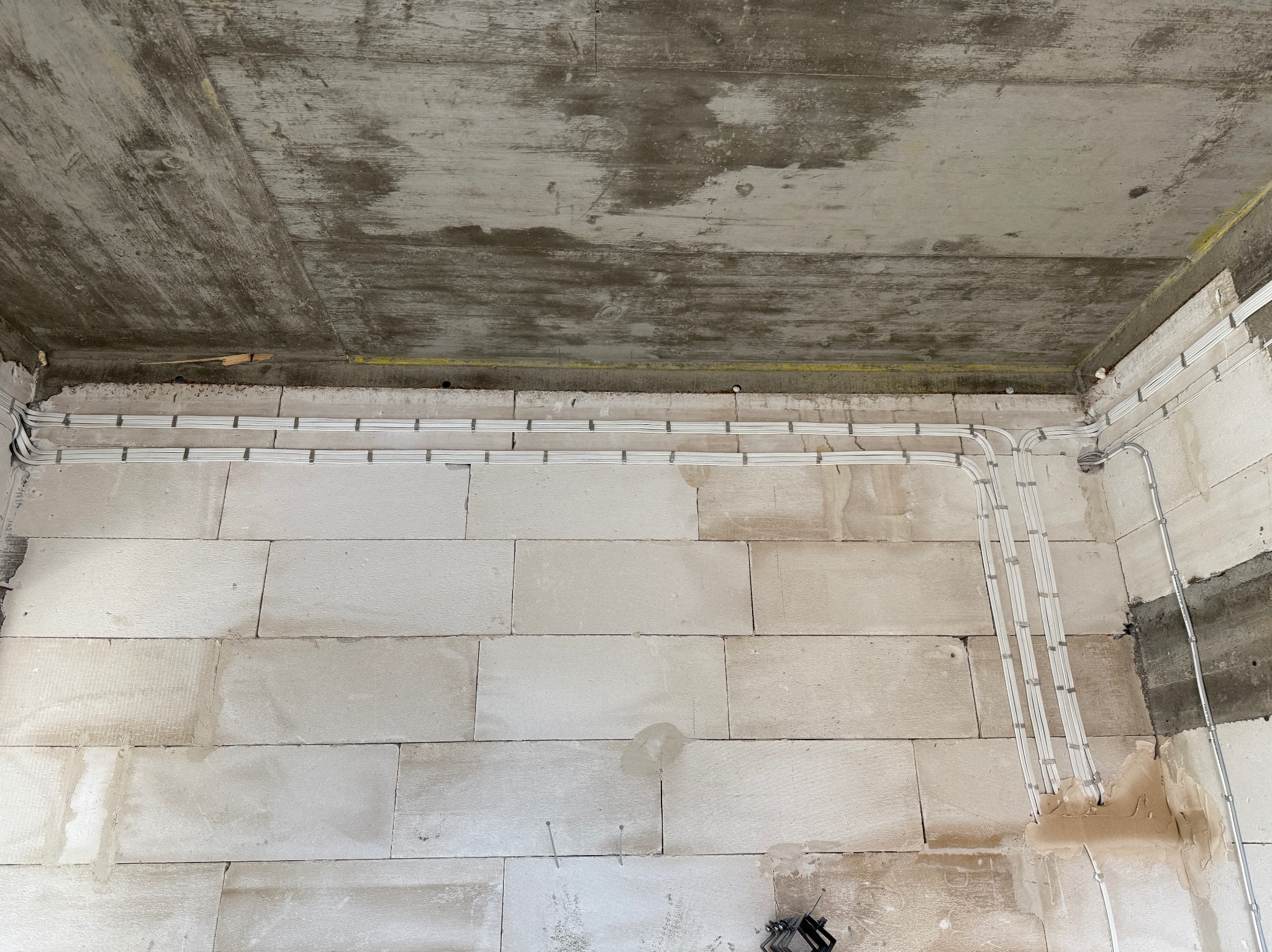 Białe kable elektryczne ułożone w rzędach na ścianie z białych bloczków, widoczne szare złącza i surowy betonowy sufit. Instalacja w trakcie realizacji.