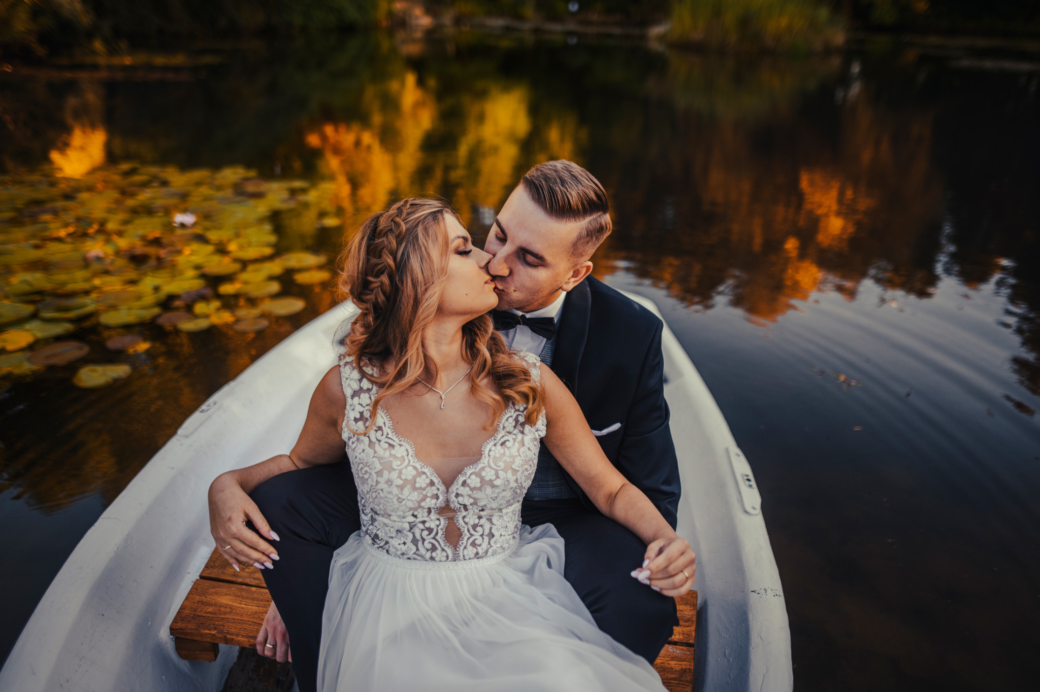 Para młoda w łódce na jeziorze, delikatny pocałunek, suknia z koronką, jesienne liście na wodzie.