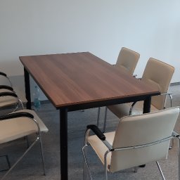 Excramm Robert Klepacki - Sala konferencyjna z prostokątnym stołem z ciemnego drewna na czarnych metalowych nogach i krzesłami z jasnej skóry z czarnymi podłokietnikami, butelka wody mineralnej pod stołem.