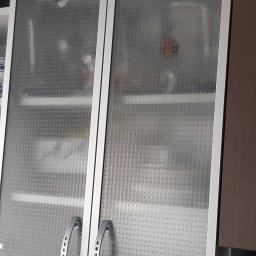 Excramm Robert Klepacki - Szklana witryna w kuchni z aluminiową ramą i uchwytami, ukazująca zawartość szafki z delikatnym wzorem na szkle.