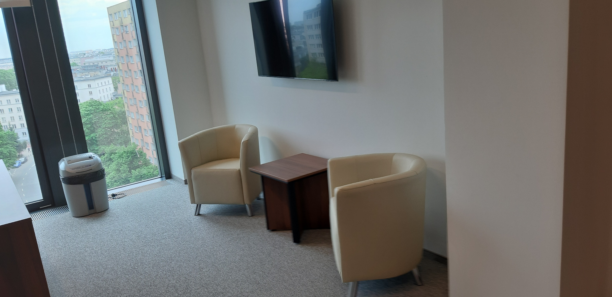 Dwa kremowe fotele klubowe i mały stolik kawowy w pokoju z dużym oknem z widokiem na miasto.