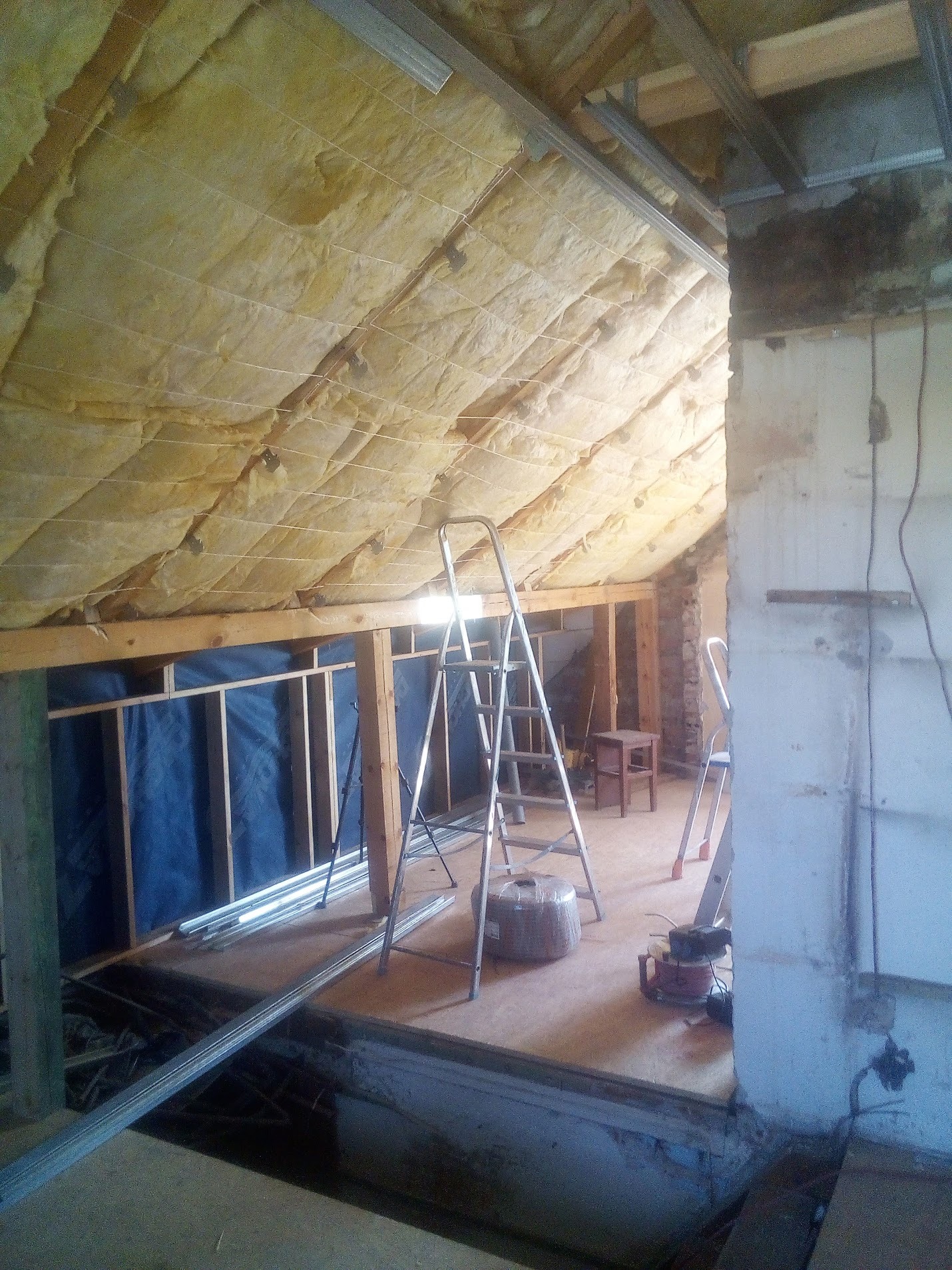 Poddasze w trakcie ocieplania wełną mineralną, widoczne metalowe profile sufitowe, drabina i narzędzia w Jarocinie.