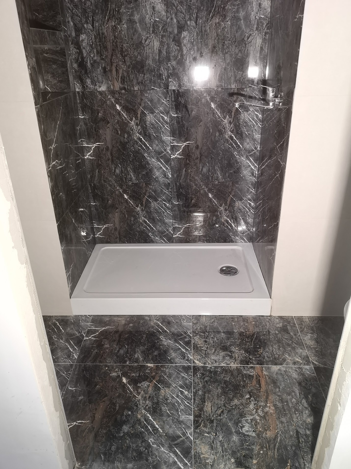 Wykończona kabina prysznicowa z czarnymi płytkami imitującymi marmur, biały brodzik i chromowana armatura, widok z góry na brodzik.