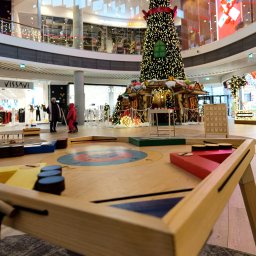 Nexturniej - atrakcje i animacje dla dzieci i dorosłych - Drewniany stół do gry w kapsle z kolorowymi polami i pionkami, ustawiony w galerii handlowej z dekoracjami świątecznymi w tle.