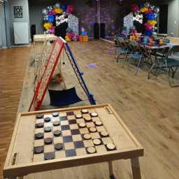 Nexturniej - atrakcje i animacje dla dzieci i dorosłych - Sala zabaw z dekoracjami urodzinowymi, stołami do gier, w tym warcaby i gra zręcznościowa z piłeczkami, przygotowana na przyjęcie.