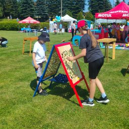 Nexturniej - atrakcje i animacje dla dzieci i dorosłych - Dwoje dzieci bawi się interaktywną, drewnianą zabawką z otworami i kulkami na trawniku podczas plenerowej imprezy.