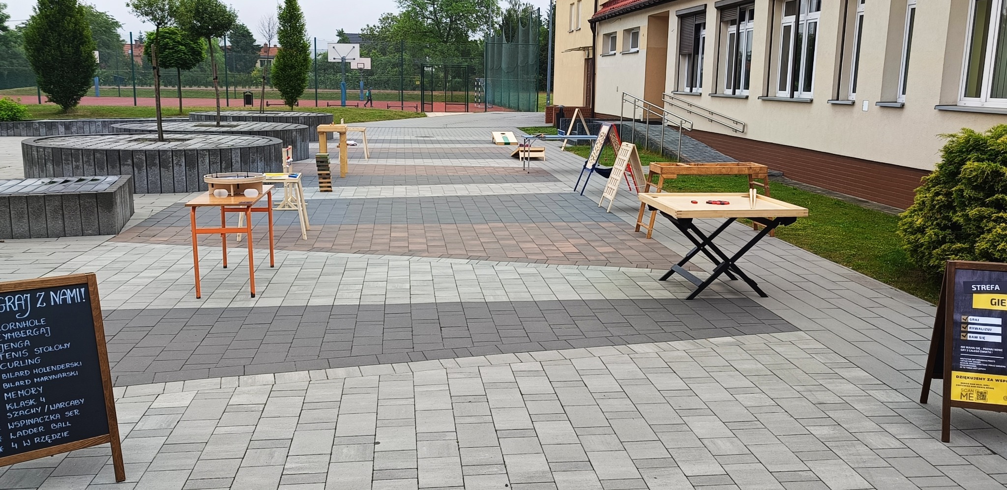 Zewnętrzna strefa gier z różnymi stanowiskami: cymbergaj, jenga, bilard holenderski, ladder ball, szachy, warcaby i inne gry na stołach na zewnątrz budynku.