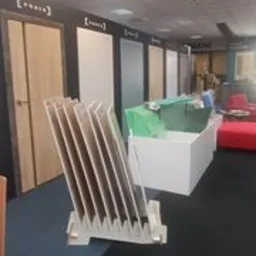 Ekspozycja różnych modeli drzwi w salonie, z widocznymi próbkami kolorystycznymi na pierwszym planie, w tle sofy i elementy wystroju.