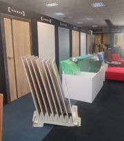 Ekspozycja różnych modeli drzwi w salonie, z widocznymi próbkami kolorystycznymi na pierwszym planie, w tle sofy i elementy wystroju.