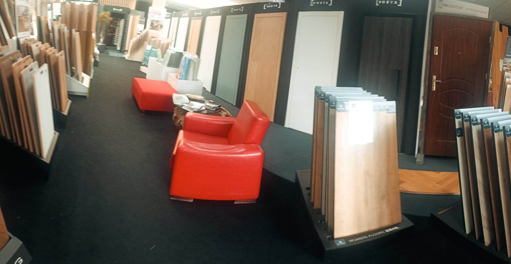 Ekspozycja w salonie z drzwiami wewnętrznymi i panelami podłogowymi, z czerwonym fotelem dla klientów.