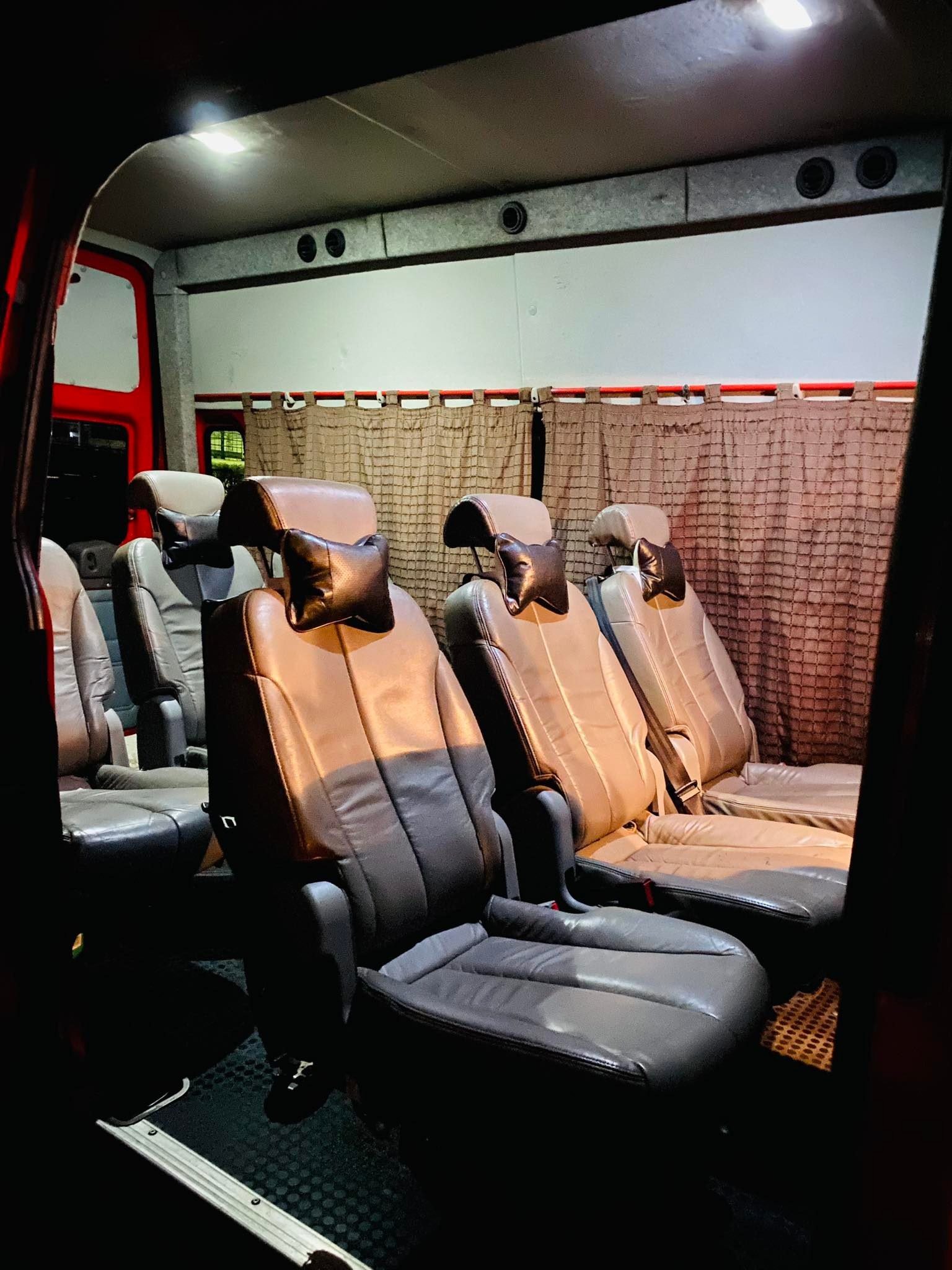 Wnętrze busa z rzędami skórzanych foteli z czarnymi zagłówkami w kształcie poduszki, zasłonięte okna z tyłu, oświetlenie sufitowe.
