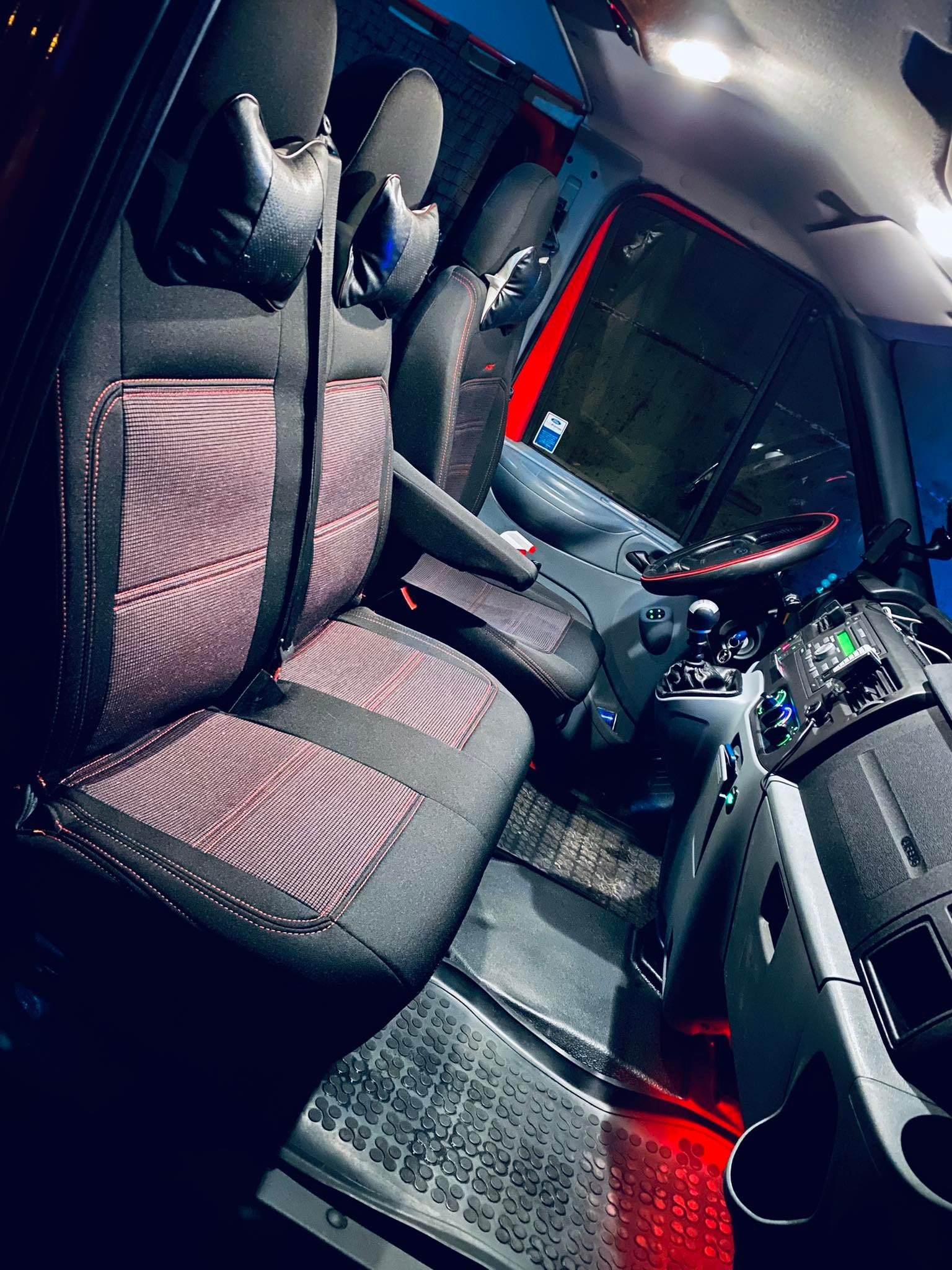 Wnętrze busa z tapicerowanymi fotelami w kolorze czarnym z bordowymi akcentami, widoczna deska rozdzielcza, podłoga z gumową wycieraczką i oświetlenie kabiny.