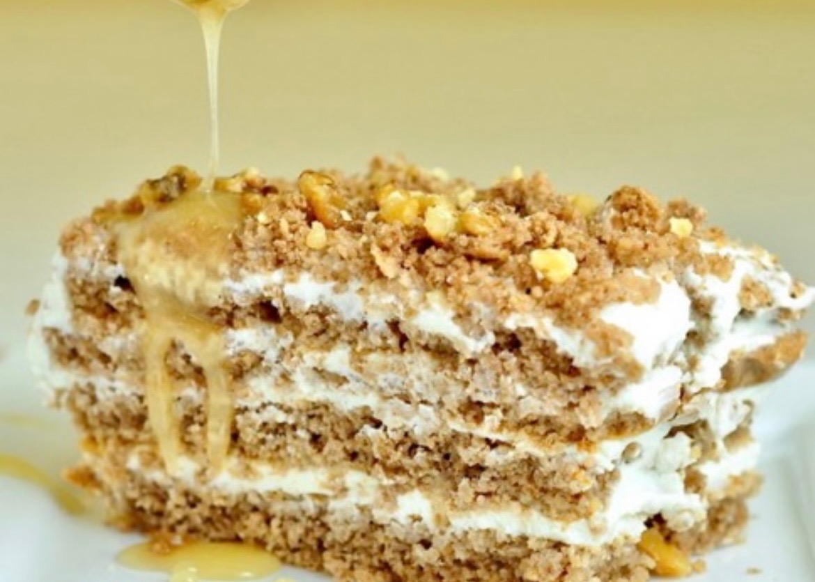 Kawałek przekładańca orzechowo-mrówkowego z widocznymi warstwami ciasta i kremu, polany syropem i posypany orzechami.