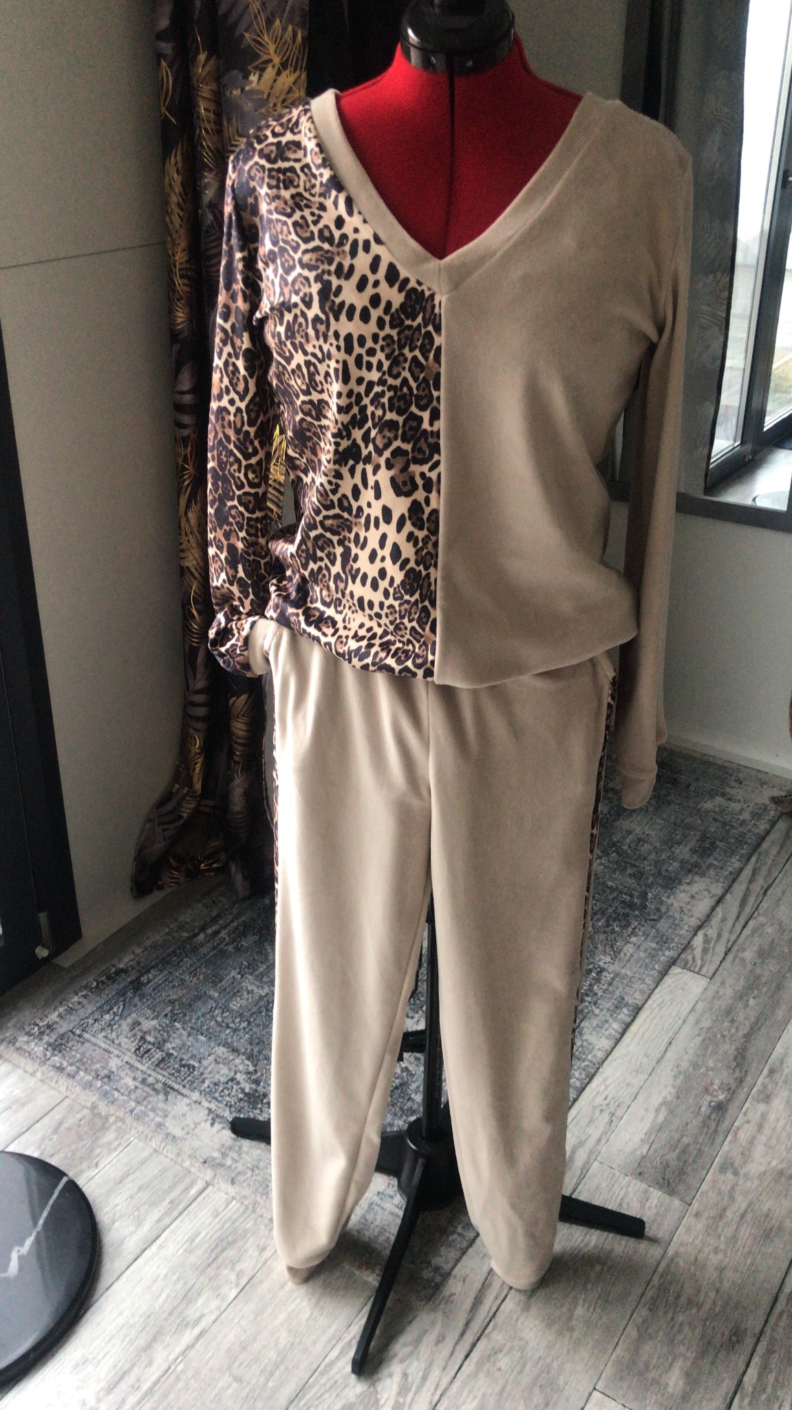 Komplet dresowy damski z długim rękawem, uszyty z dwóch rodzajów materiałów: beżowego oraz w panterkę, prezentowany na czerwonym manekinie krawieckim.