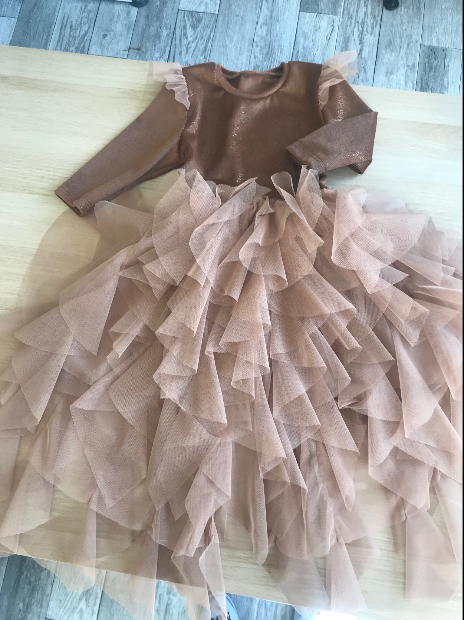 Brązowa sukienka z długim rękawem i tiulową spódnicą z falbanami leżąca na drewnianym podłożu.