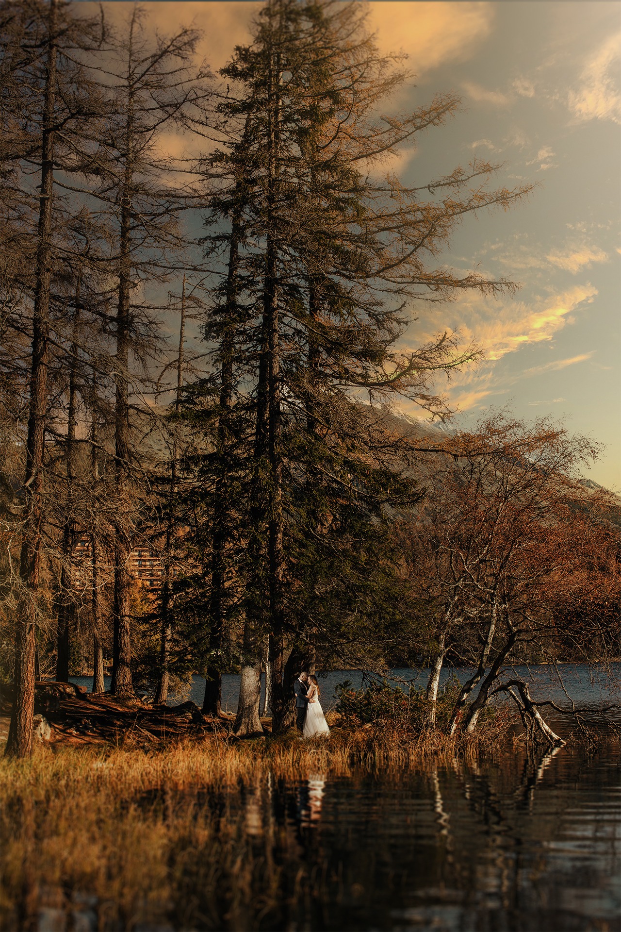 Para młoda w objęciach, w lesie nad jeziorem, w tle góry i pochmurne niebo, odbicie w wodzie