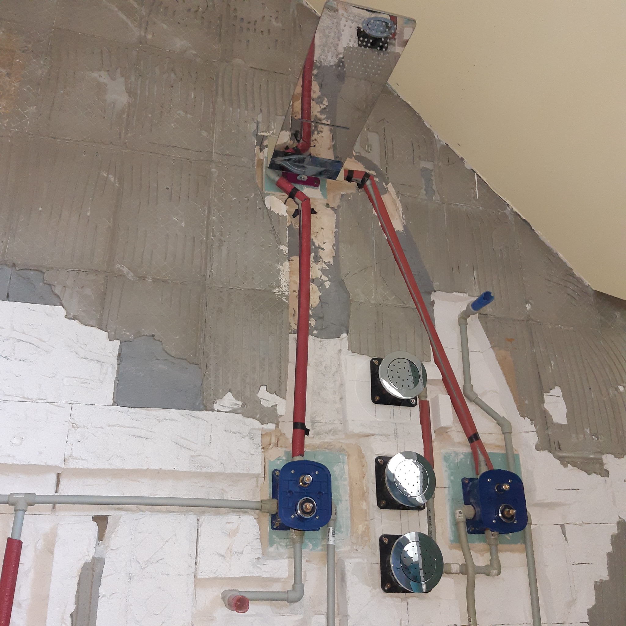 Instalacja podtynkowa prysznicowa z rozłożonymi rurami w ścianie łazienki w trakcie remontu, widoczne nieotynkowane ściany z fragmentami starej glazury.