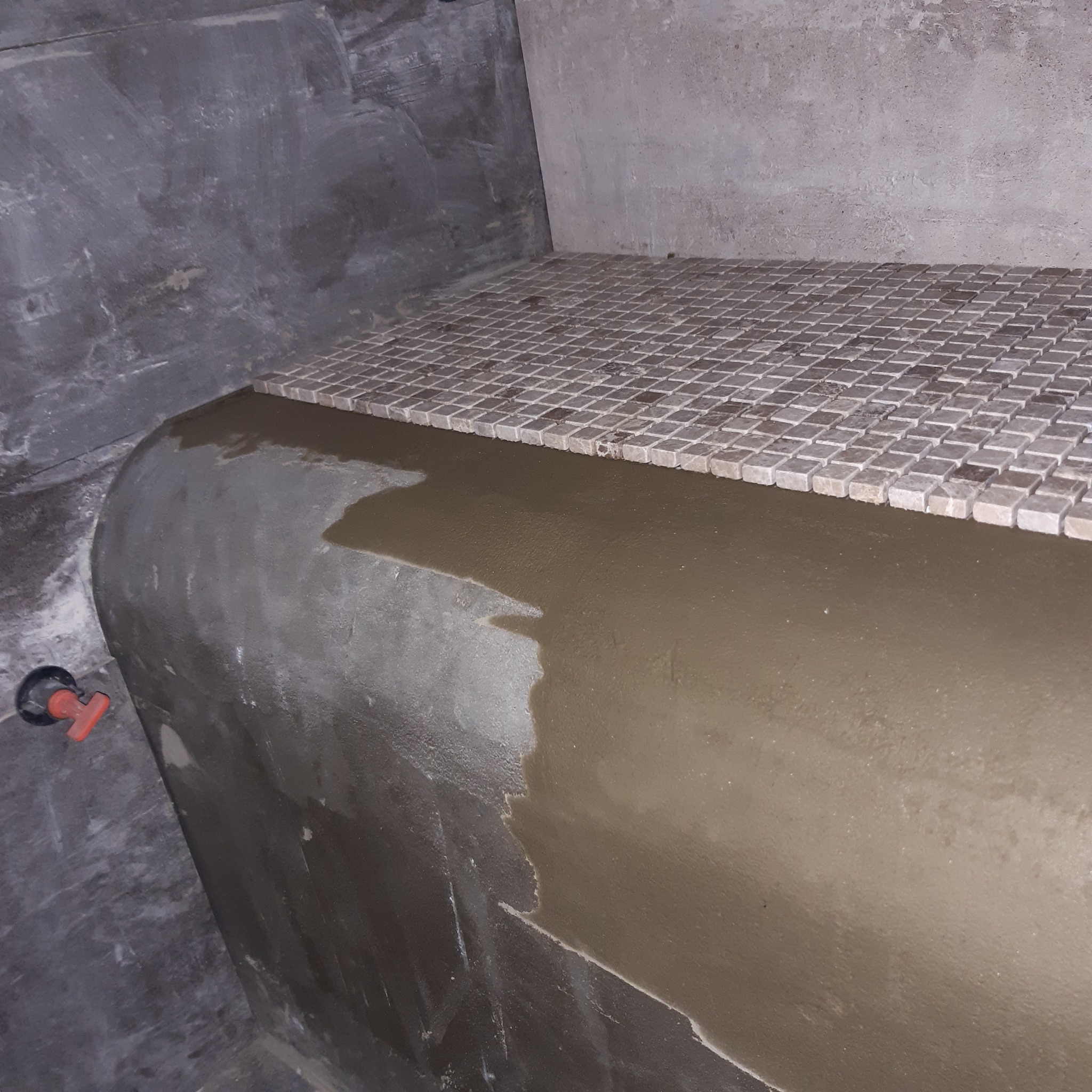 Przygotowanie do układania mozaiki na zaokrąglonej powierzchni w łazience, widoczny świeży klej i fragment ułożonej mozaiki.