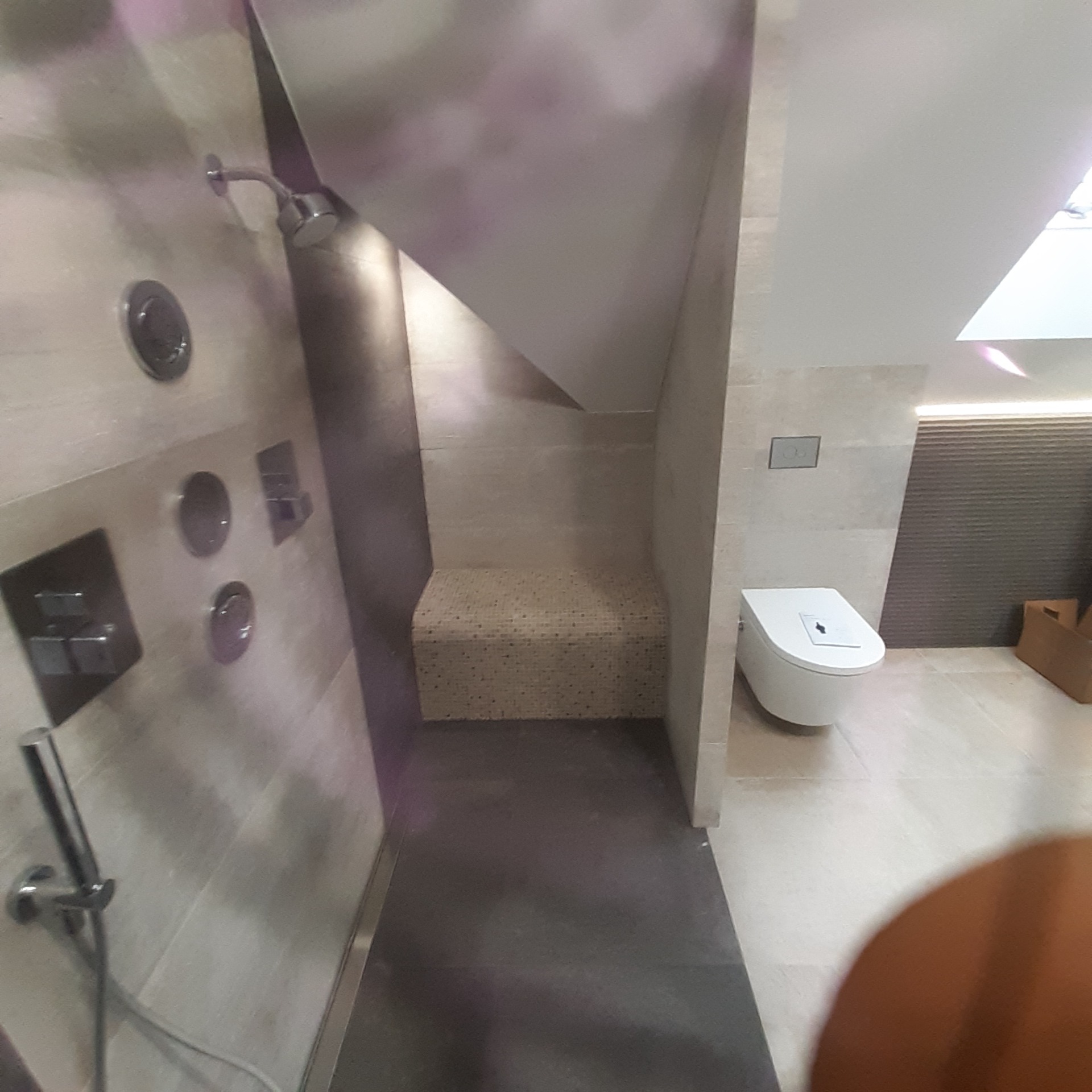 Nowoczesna łazienka z kabiną prysznicową typu walk-in, mozaikowym siedziskiem, podtynkową armaturą i wiszącą toaletą.