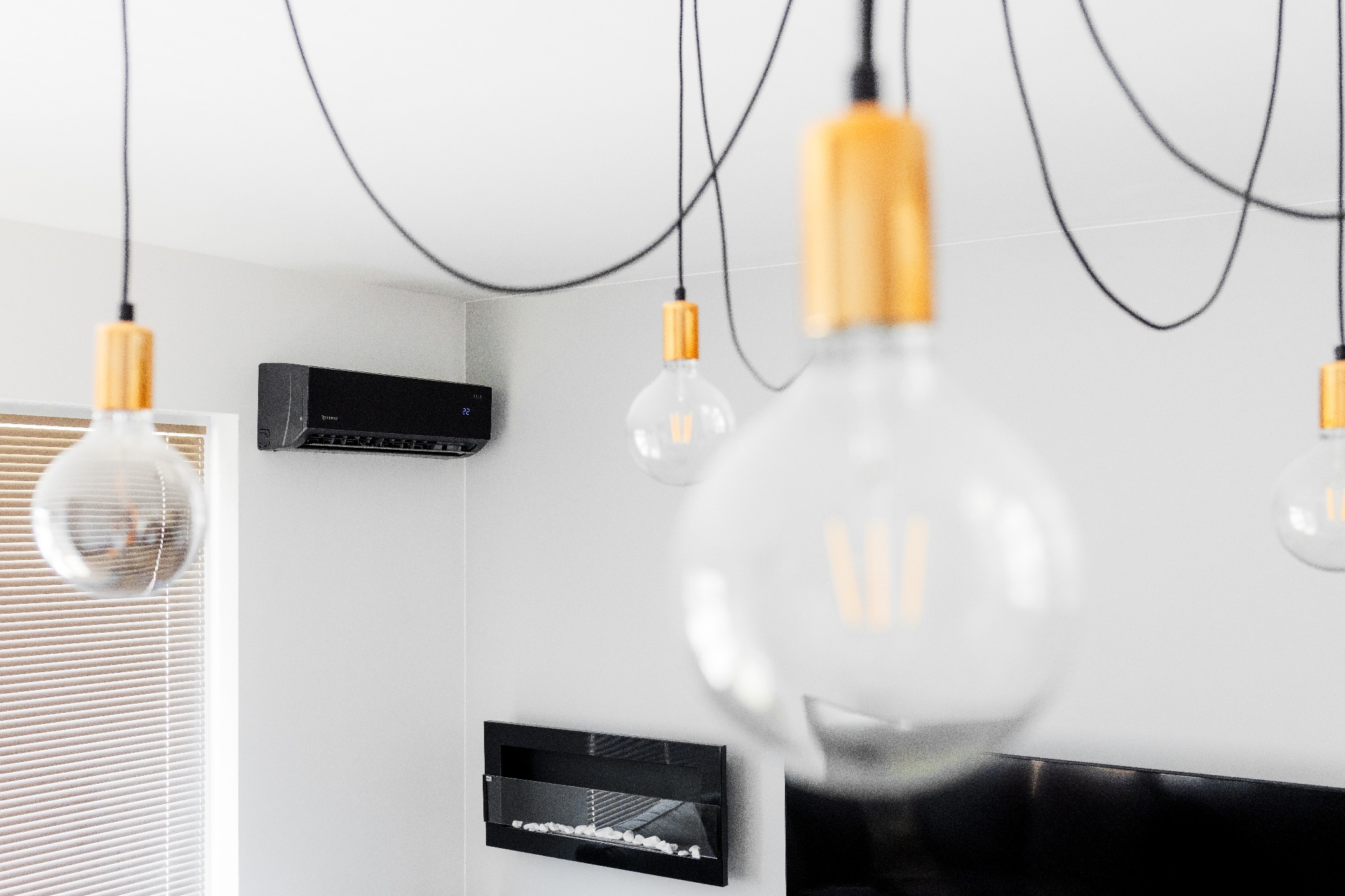 Czarny klimatyzator ścienny z wyświetlaczem temperatury 22 stopnie Celsjusza zawieszony w nowoczesnym wnętrzu, oświetlonym wiszącymi żarówkami Edison z elementami drewna i czarnym kablem,...