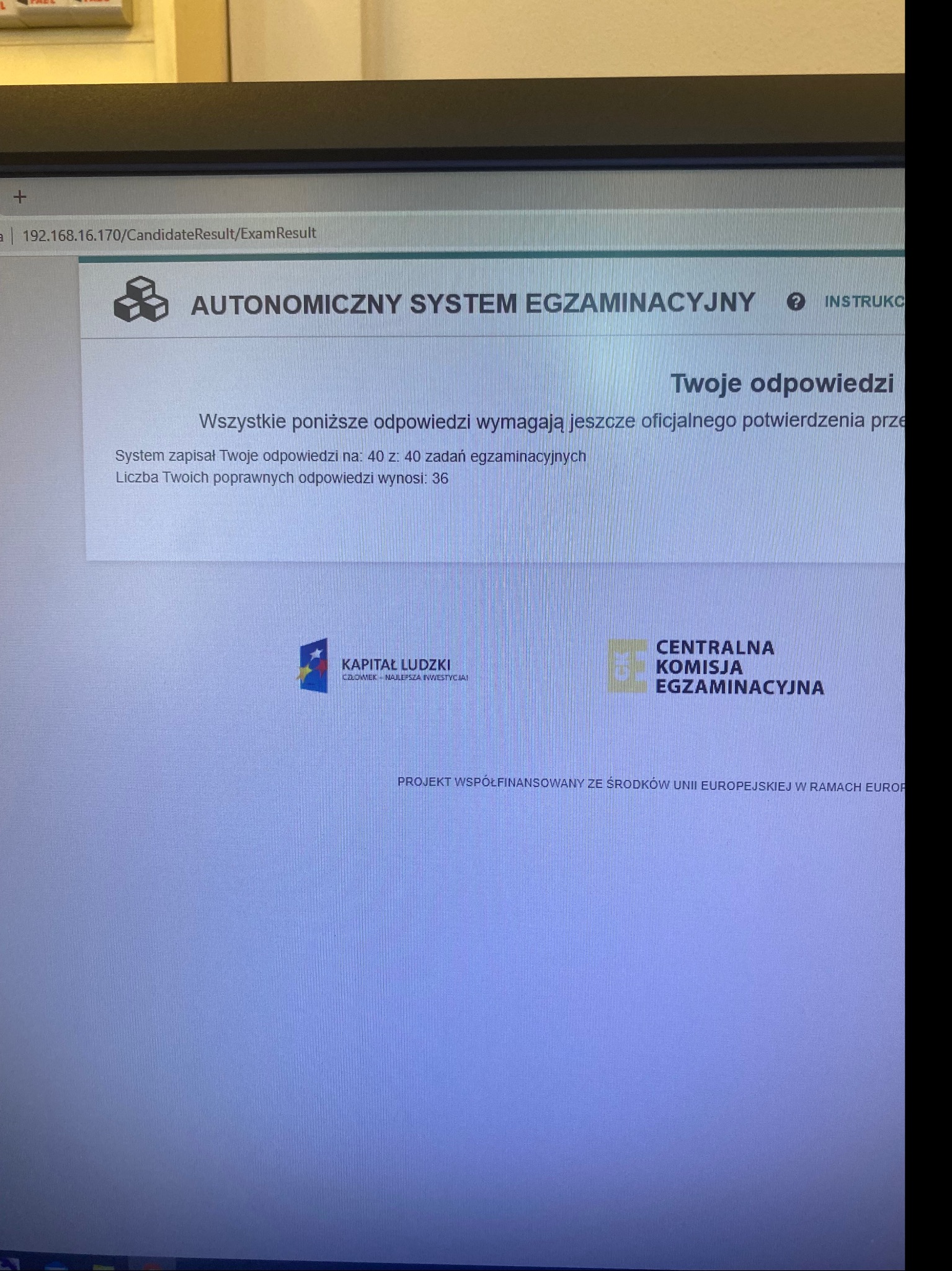 Ekran komputera wyświetlający wynik egzaminu online z informacją o liczbie poprawnych odpowiedzi i logotypami instytucji egzaminacyjnych oraz programów finansujących.